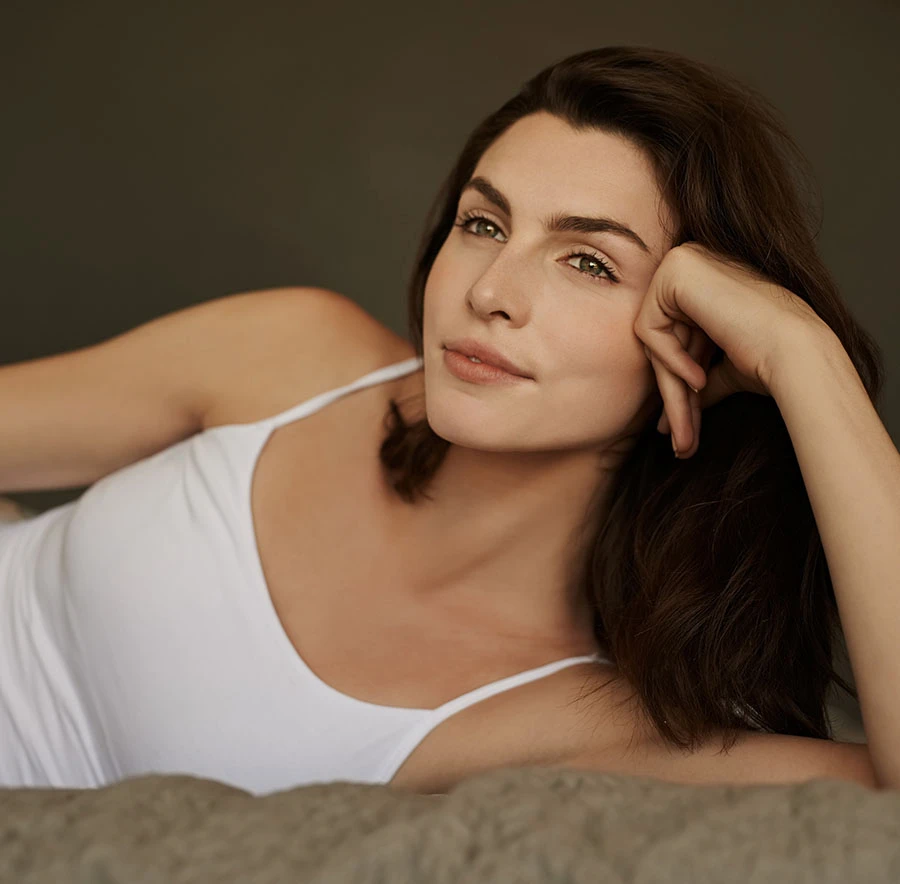 Brunette woman lying on bed in a white tank top, relaxing - Chemical Peels in Toronto, Canada