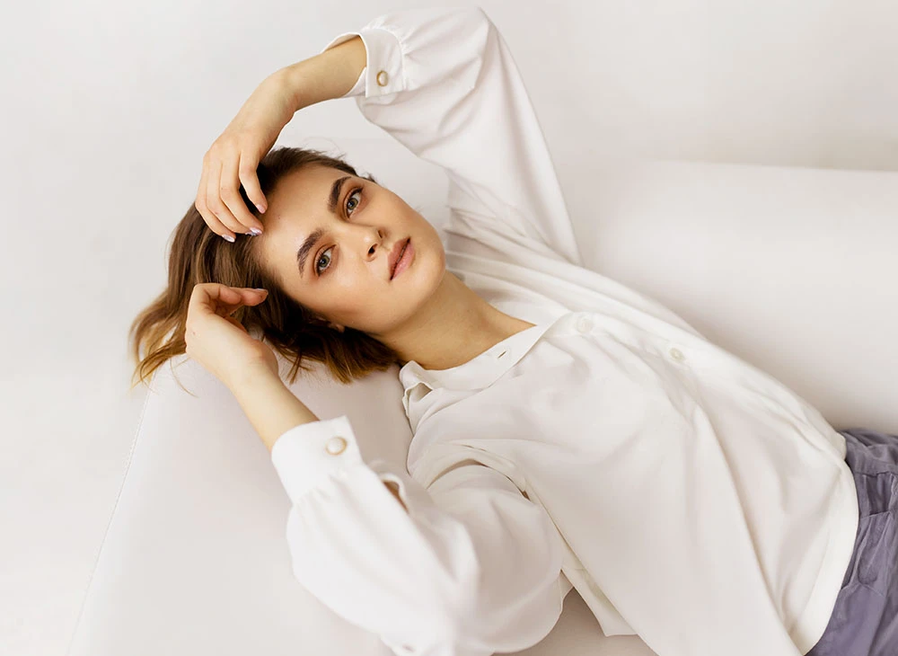 woman in white shirt leaning back on couch | Edelstein Cosmetics