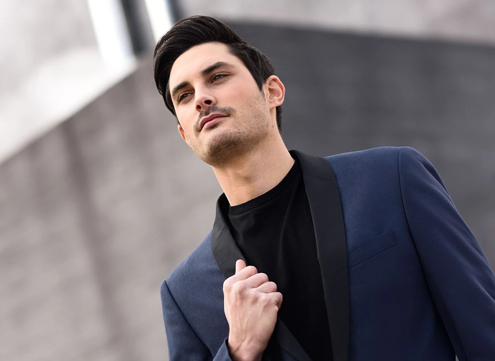 A brunette man in a navy blazer, posed in an urban setting - Otoplasty Procedure in Toronto, Canada